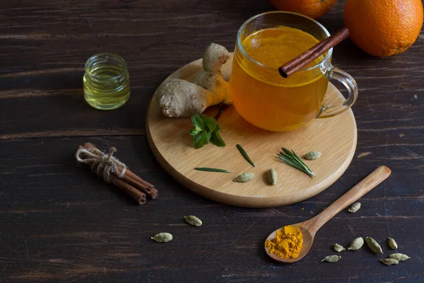 Té de jengibre con azafrán en un vaso Copa e ingredientes en una mesa de madera oscura — Foto de Stock