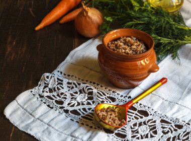 Karabuğday lapası tencerede, ahşap kaşık keten peçetede, sebze arka planda.