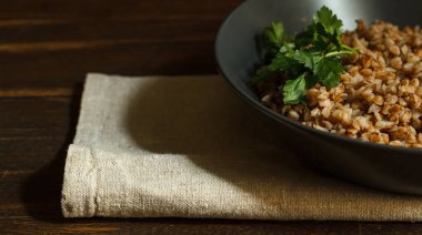 Koyu seramik tabakta yeşil buğday lapası keten peçeteye yakın, koyu ahşap arka planda, yatay olarak.