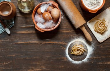 Tahtada unlu ev yapımı makarna, yumurtalı bir kase, ahşap arka planda merdane ve pişirme malzemeleri, uzay manzaralı üst manzara.