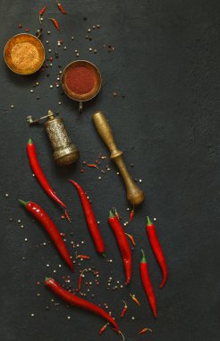 Kırmızı biber kabukları, kurutulmuş bebek paprika ve biberli bakır mutfak aletleri, siyah bir masanın üstündeki baharatlar.