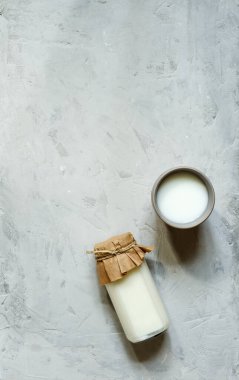 Kağıt kapaklı servis şişesi, iple bağlanmış bir bardak süt gri taştan arka planda, üst manzaralı boşluk.
