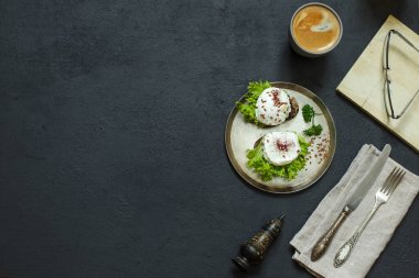 İki haşlanmış yumurta ve bakır tabakta yeşil salata, kahve, kitap ve okuma gözlüğü.