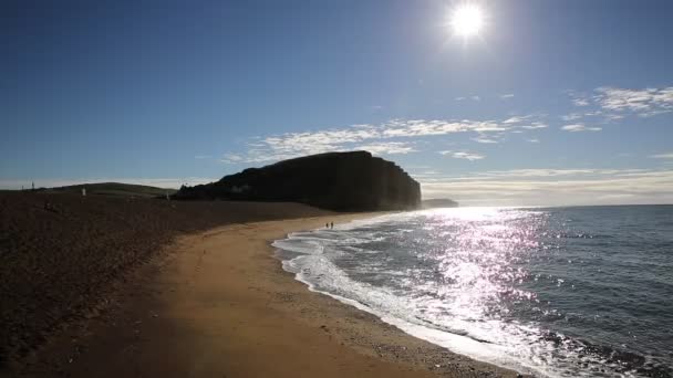 Jurassic coast Dorset at West Bay uk in morning with sun shining on shimmering sea and distant people going swimming — Stock Video