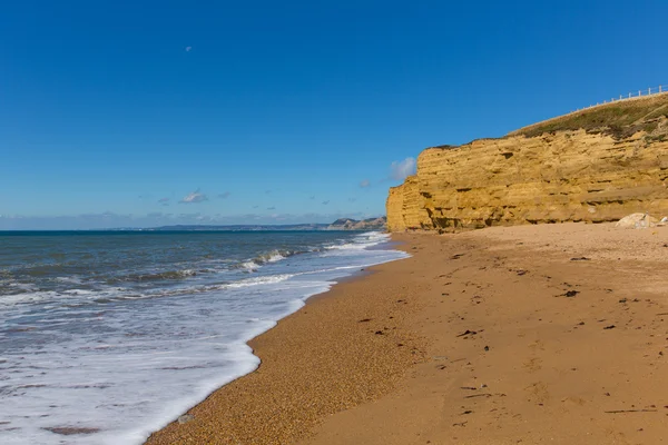 UK Jurassic coast plaża Burton Bradstock Dorset w Anglii z skały piaskowcowe i białe fale w lecie błękitne morze i niebo — Zdjęcie stockowe