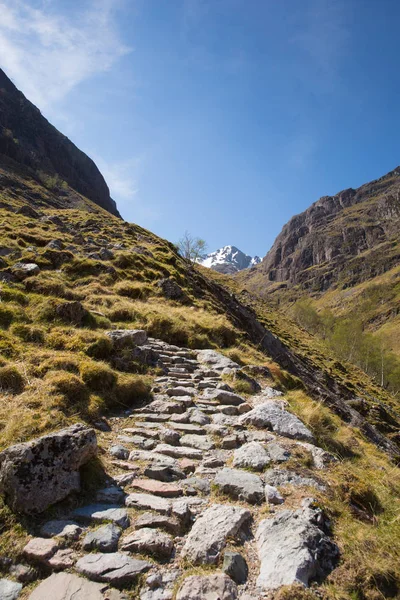 Path up to Glencoe snow topped mountains Scotland UK in Scottish Highlands in spring with blue sky and sunshine