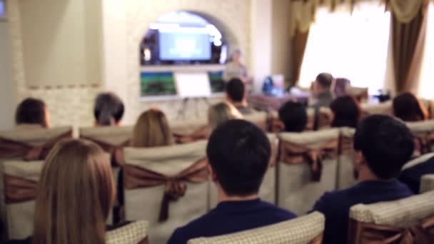 年轻人在网络营销的介绍 在酒店大厅进行网络营销的比特币培训 人们在电视上观看演讲 听演讲者 — 图库视频影像
