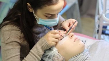Kalın, gür kirpik gözlerinin önünde. Profesyonel master yapmak uzun kirpiklere cımbız bir istemciye bir çift uzatarak. Kirpik uzatma güzellik Studio.