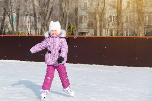 The little girl laughs and skates on the ice.