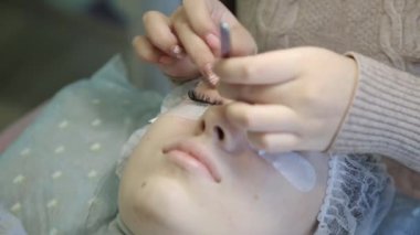 Genç bir kız bir güzellik salonu kirpik artırır. Sarışın kız artan ve hacimsel kirpik uzantıları süreci.