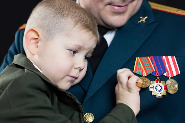 Um menino pequeno de uniforme militar olha para as medalhas militares . — Fotografia de Stock