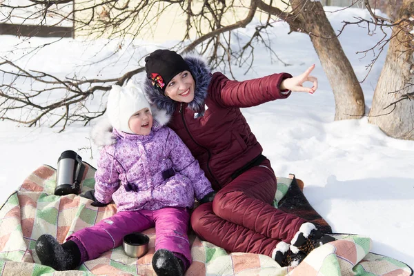 Mamá y su hija están sentadas en un cuadros en la nieve en el invierno . — Foto de Stock