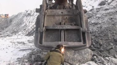 Bir çalışma metal kaynakçı bir taş ocağında çalışıyor. Kaynak maskesi ve bir elektrot yardımıyla tulum işçi Ekskavatör Kepçe onarır.