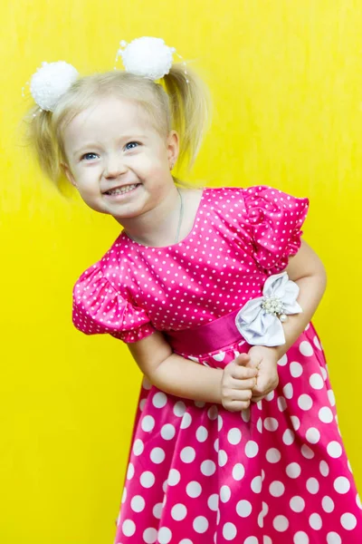 Piękna mała Blondynka w czerwonej sukience z kropki z kwiatkiem na żółtym tle. — Zdjęcie stockowe