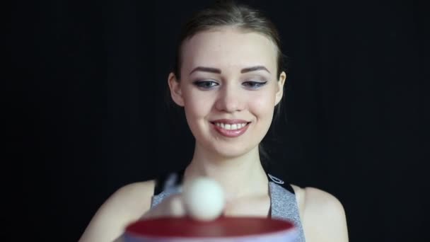 一个穿着运动服的漂亮女孩在网球拍上掷球 运动员笑着看着打乒乓球的球 — 图库视频影像