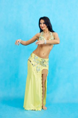 Büyüleyici dansçı oryantal göbek dansı mavi bir arka plan üzerinde gerçekleştirir..