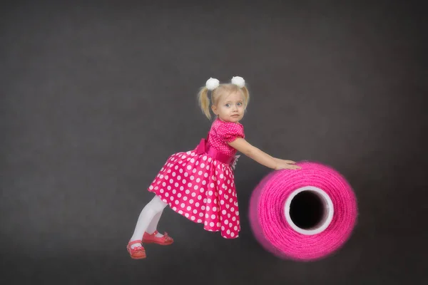 Uma menina bonita pequena rola um emaranhado de linha de costura . — Fotografia de Stock