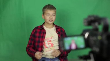 Teen video blogger yeni bir video vuruyor. Bir video kamera önünde genç bir sarışın çocuk haber yeşil bir arka plan üzerine söyler..