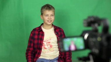 Teen video blogger yeni bir video vuruyor. Bir video kamera önünde genç bir sarışın çocuk haber yeşil bir arka plan üzerine söyler..