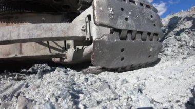 Ağır bir traktörün tırtılı bir taşa çarpar. Ağır bir kazıcı yolda taşa biner ve onu ezer..