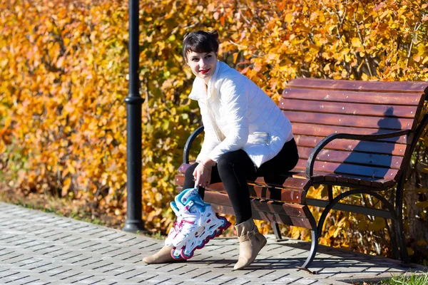 Une fille avec des patins à roulettes dans ses mains s'assoit . — Photo