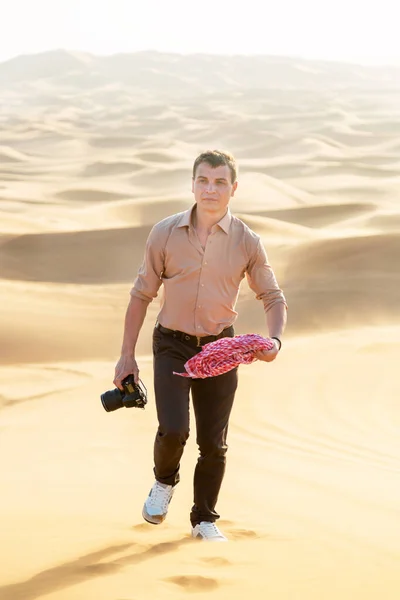 写真家はカメラを手に砂漠を歩いている 結婚式の写真撮影のために砂漠の砂の中を歩く男性写真家 — ストック写真