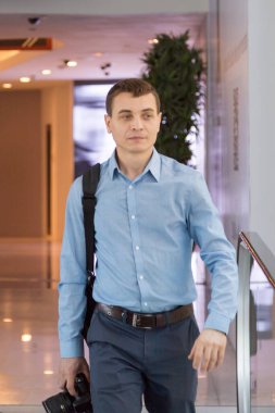 Elinde kamera olan bir adam alışveriş merkezinden geçenler arasında. Bir erkek fotoğrafçı bir binanın içinde insanların arasında yürüyor..