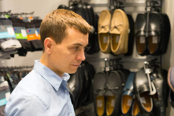 Caucasian male shopper in blue clothes chooses shoes in a shopping supermarket A man chooses shoes in a store.