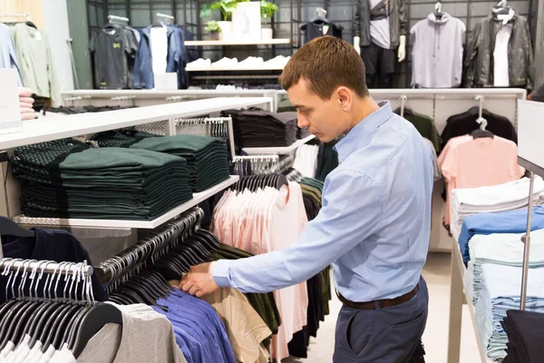 stock image A man chooses outerwear in a store. An adult Caucasian man looks among the rows of clothes on a hanger his suitable size of clothes.