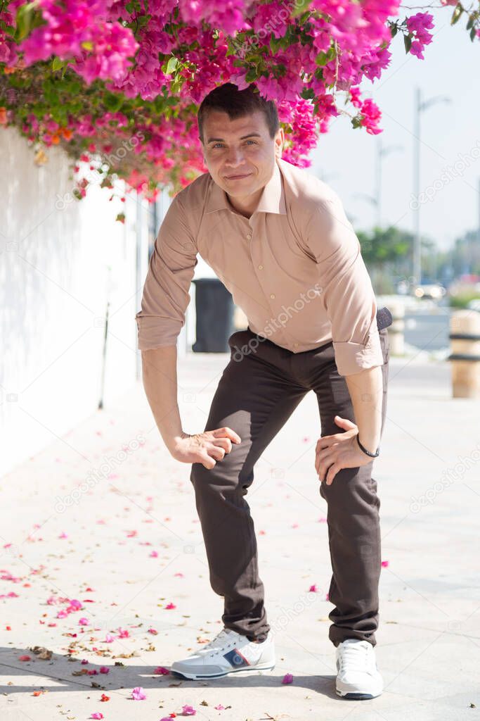 A man near a beautiful flowering tree. European tourist in the shadow of  large tree branch with bright red flowers