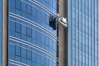 Bir işçi çok katlı bir binanın camını yıkar. Şehirdeki gökdelenlerin camlarını temizlemeye çalış..