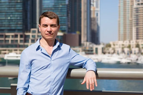 Handsome young man on the background of skyscrapers. Caucasian man 30-35 years old in a blue shirt on a background of tall buildings.