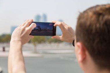 Turist akıllı telefondan video çeker. Bir adam elinde telefon tutuyor, yüksek binaların fotoğraflarını çekiyor..