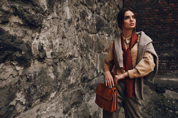 Женщина в модной одежде позирует у стены
