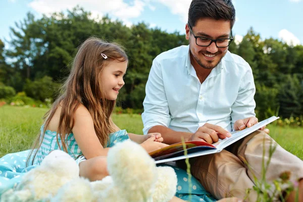Pai leitura criança um livro no parque. Pai e filha na natureza — Fotografia de Stock