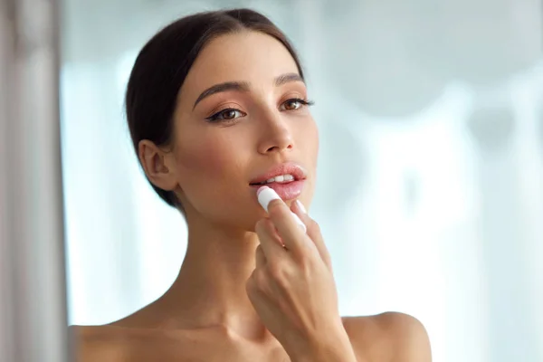 Mooie vrouw met schoonheid gezicht past balsem op de lippen. Huidverzorging — Stockfoto