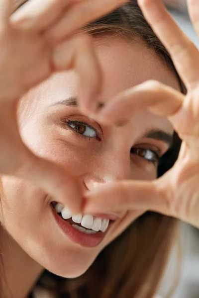 Bella donna felice mostrando segno d'amore vicino agli occhi . — Foto Stock