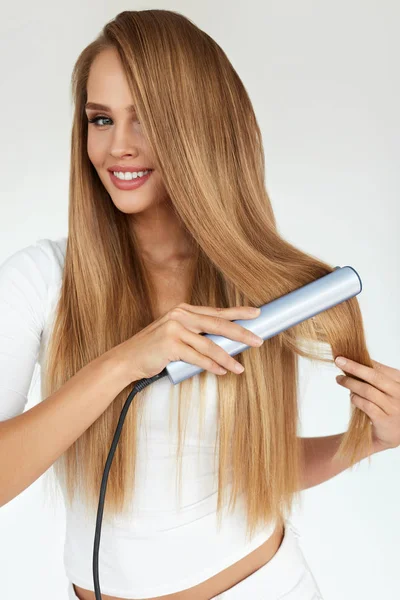 Fryzjerskie. Kobieta z piękne długie włosy przy użyciu prostownicy — Zdjęcie stockowe