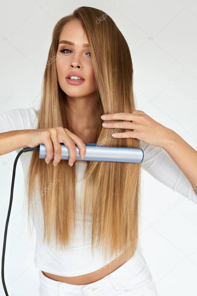 Hairdressing. Woman With Beautiful Long Hair Using Straightener
