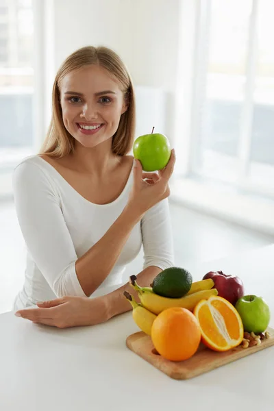 Beautiful Woman Holding Apple In Kitchen With Fruits On Table