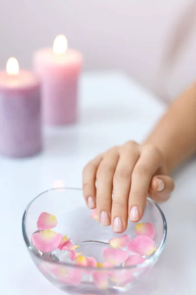 Mujer mano en baño de aroma. Uñas empapadas en agua con flores — Foto de Stock