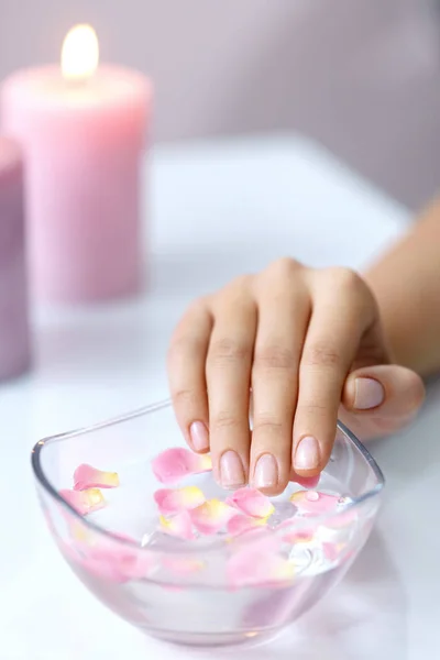 Femme main dans le bain d'arôme. Ongles trempant dans l'eau avec des fleurs — Photo