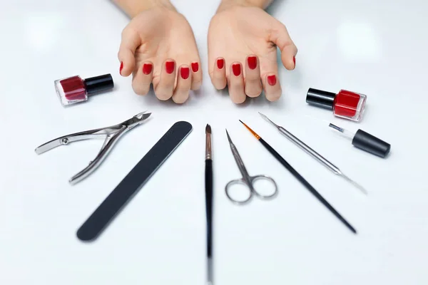 Cuidado de las uñas. Manos de mujer con esmalte de uñas rojo y herramientas de manicura — Foto de Stock