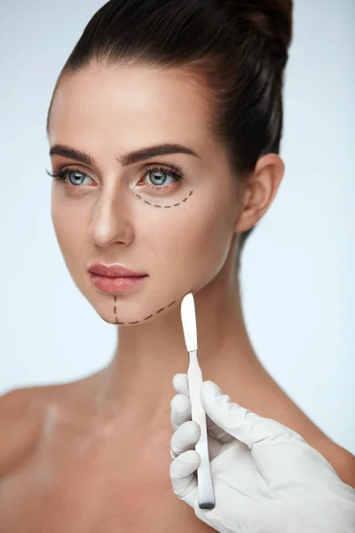 Nahaufnahme der Hand einer Kosmetikerin mit Skalpell in der Nähe des Gesichts einer jungen Frau — Stockfoto
