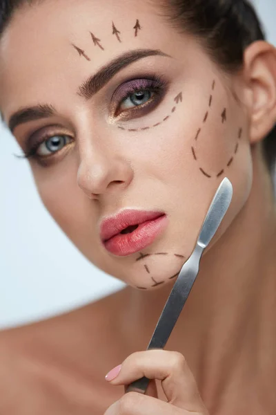 Giovane donna con linee chirurgiche sul viso e bisturi in mano — Foto Stock