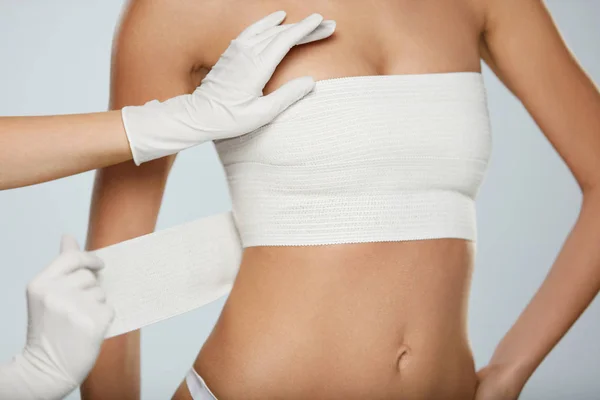 Cirurgia Plástica. Médico mãos embrulhando mama feminina em bandagem — Fotografia de Stock