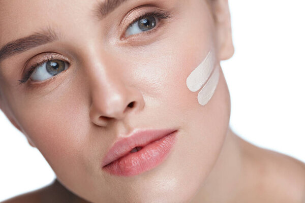 Уход за кожей. Сексуальная девушка с основанием или косметическим кремом на лице
