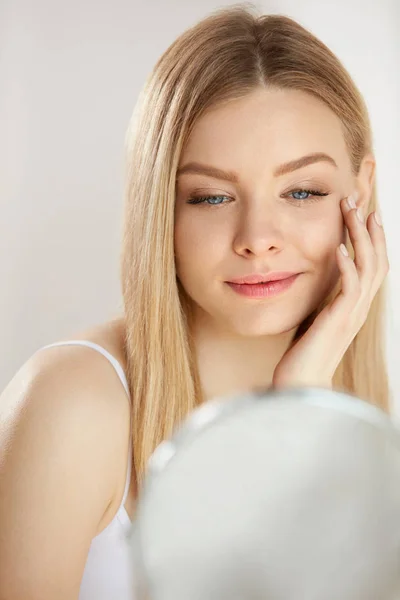 Schönheit Gesichtspflege. Mädchen mit gesunder Haut schaut in den Spiegel — Stockfoto