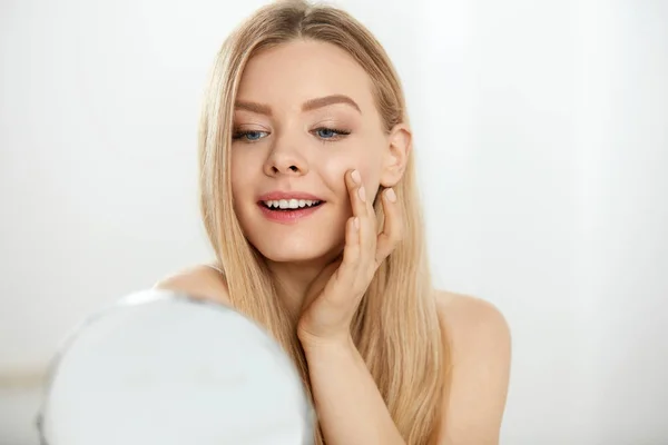 Maquillaje y belleza. Mujer tocando la piel de la cara mirando en espejo — Foto de Stock