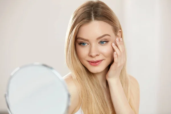 Maquillaje y belleza. Mujer tocando la piel de la cara mirando en espejo — Foto de Stock